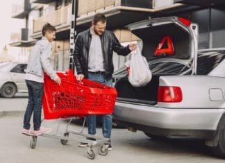 Mężczyzna z chłopcem pakują torby do bagażnika auta na parkingu